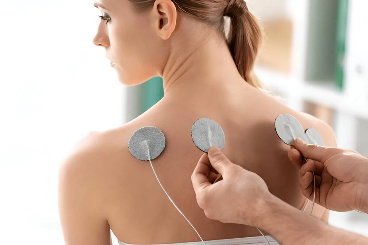 Therapist setting electrodes on back of woman during electrode treatment