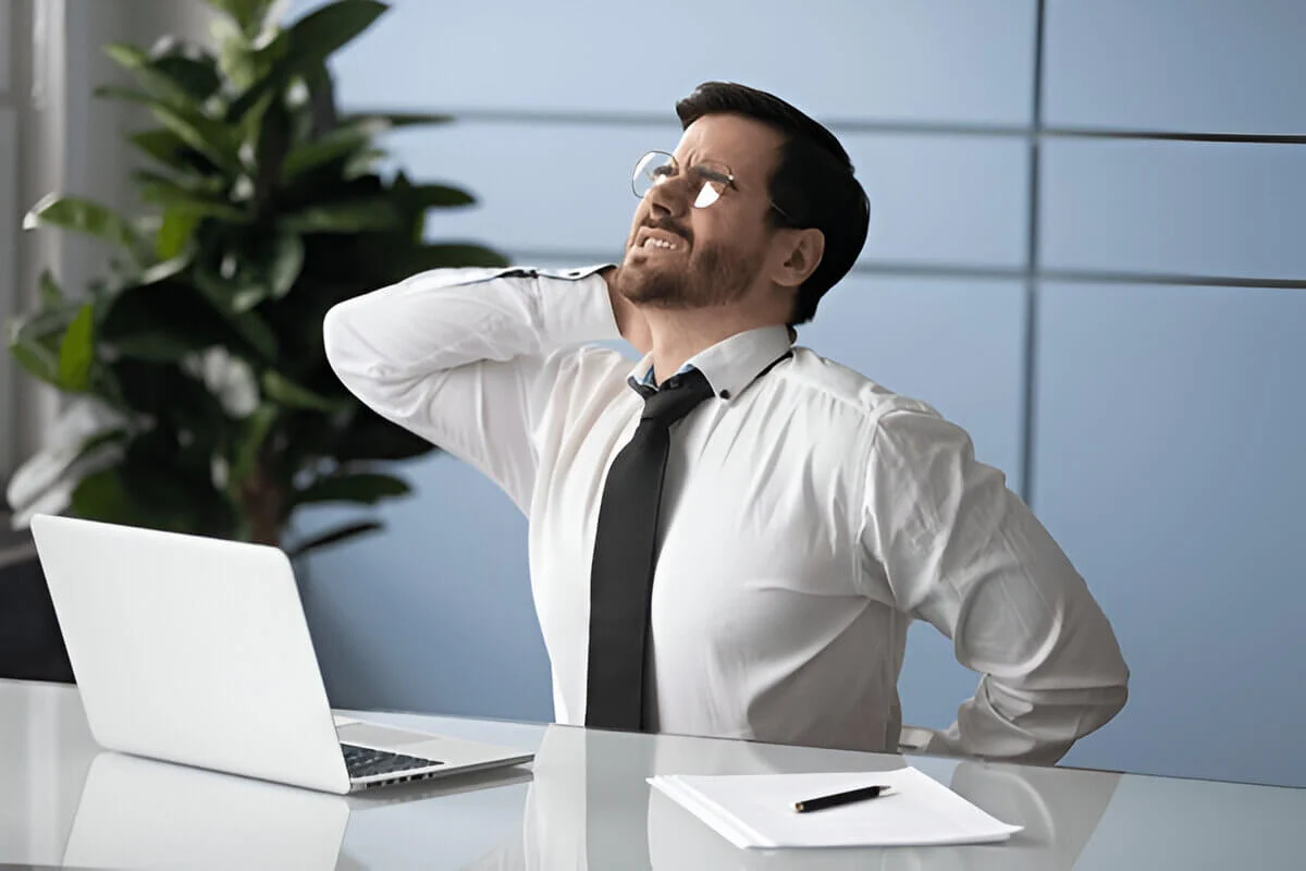 Unhealthy young manager sitting at table with laptop suffering from strong muscle back pain due to sitting work at office