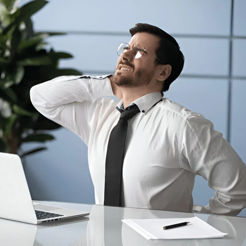 Unhealthy young manager sitting at table with laptop suffering from strong muscle back pain due to sitting work at office